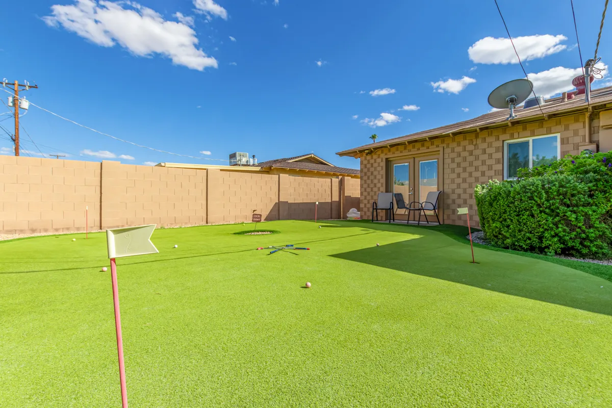 An inviting outdoor putting green surrounded by lawn chairs and lush landscaping, perfect for casual mini-golf and relaxed gatherings. The playful setting encourages pre-evening fun and socializing in a private, homey environment.