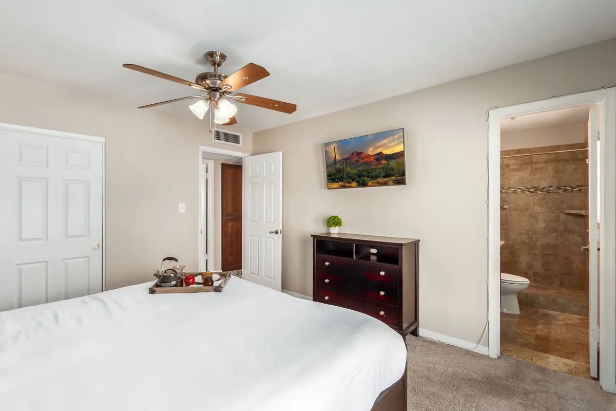 A quiet, relaxing bedroom with a neatly made bed, a dresser, artistic touches on the wall, and doors to another space. The design is simple but stylish, providing a sense of calm and privacy.