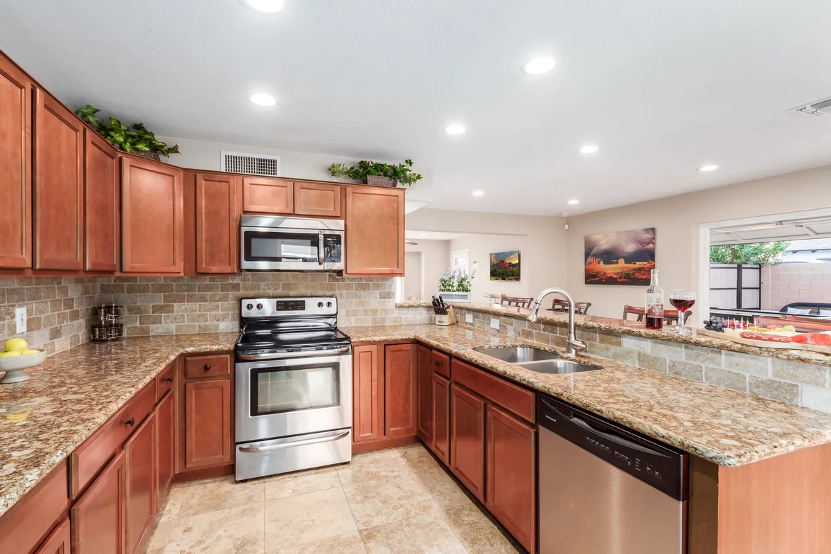 A spacious kitchen featuring granite countertops, stainless steel appliances, wooden cabinets, and a central island, all bathed in warm, welcoming lighting. Ample workspace is complemented by modern amenities, inviting both casual breakfasts and lively meal preparations.