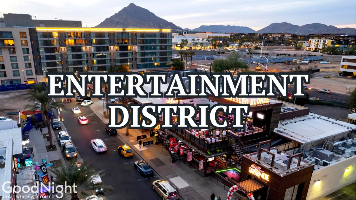The heart of the Entertainment District, featuring prominent signage, lively street activity, outdoor dining areas, and a view of surrounding mountains in the distance. The atmosphere buzzes with energy as people gather to dine, shop, and enjoy nightlife.