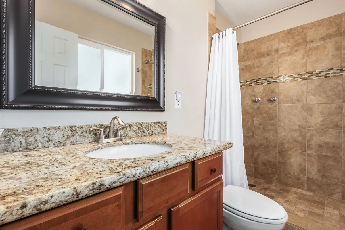 A modern bathroom featuring a granite countertop, a large mirror, and a glass-enclosed shower area. The neutral colors and minimalist decor create a spa-like, hotel-inspired atmosphere.
