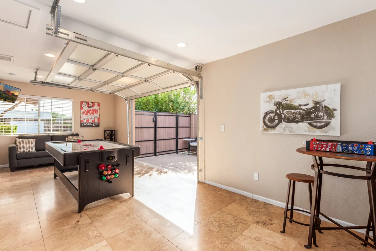 A stylish, casual game room setup with an air hockey table, sofa for spectators or relaxation, a garage door backdrop, and motorcycle artwork, creating a modern, playful vibe perfect for group gatherings and friendly competition.
