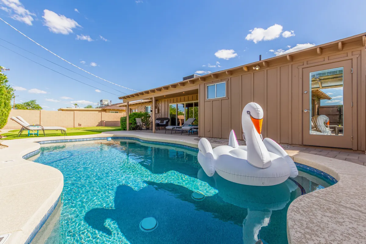 The hero image showcases a sparkling swimming pool featuring a whimsical inflatable swan, surrounded by inviting loungers and a stylish patio area. The house’s modern exterior frames the sun-drenched scene, hinting at playful, leisurely afternoons and memorable outdoor gatherings.