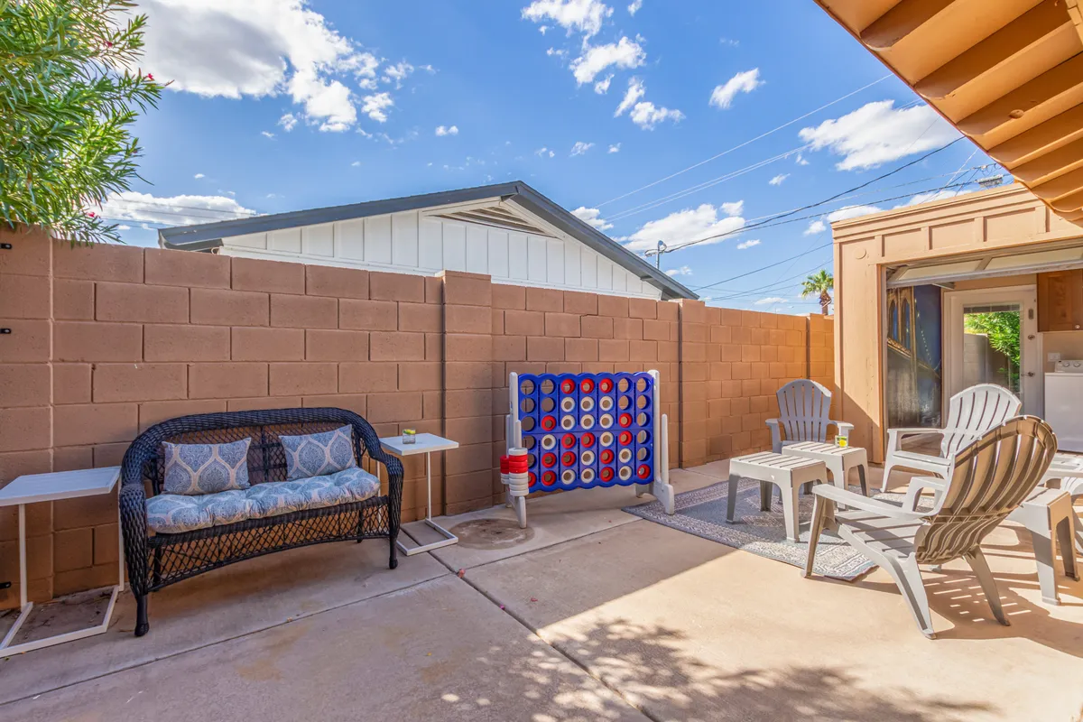 This image features an outdoor patio with a wicker sofa, a large blue connect-four game, and patio chairs. The setting is casual and friendly, highlighting spaces for both relaxation and social interaction.
