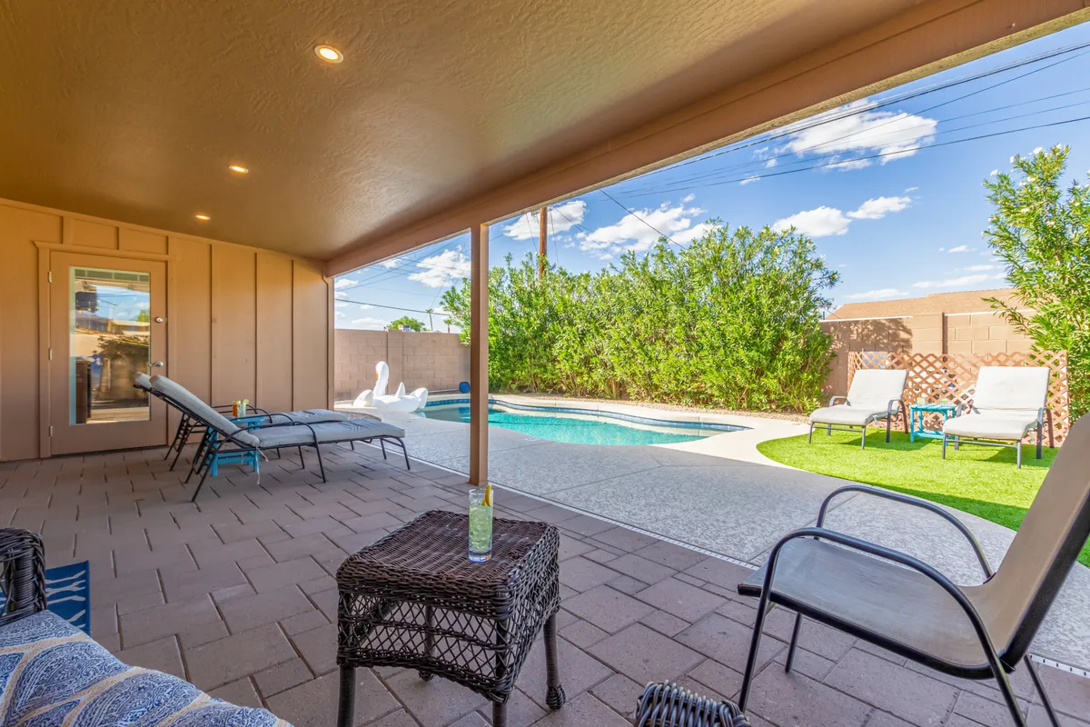 This image showcases a beautiful swimming pool area surrounded by lounge chairs and greenery, with a spacious patio area to the side. The tranquil and inviting mood captures the essence of a private resort-style backyard.